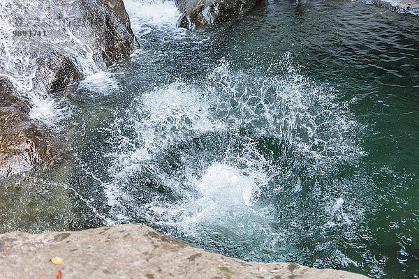 Ein Spritzer von jemandem  der in ein Schwimmloch im Wald mit einem Wasserfall springt.