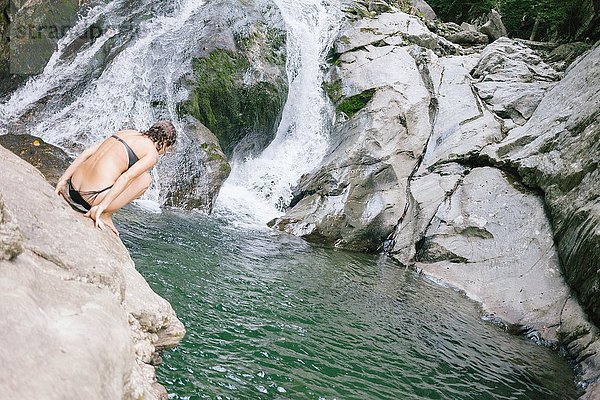 Eine Frau  die darüber nachdenkt  mit einem Wasserfall in ein Schwimmloch im Wald zu springen.