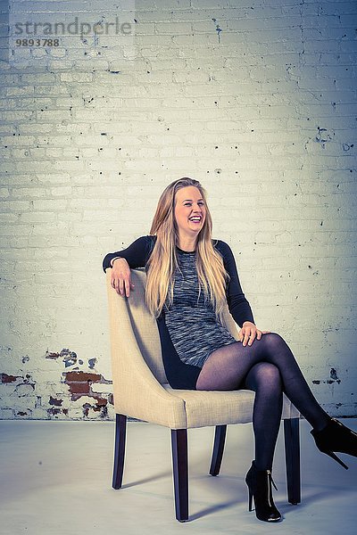 Studio-Porträt einer lachenden jungen Frau  die auf einem Stuhl sitzt.