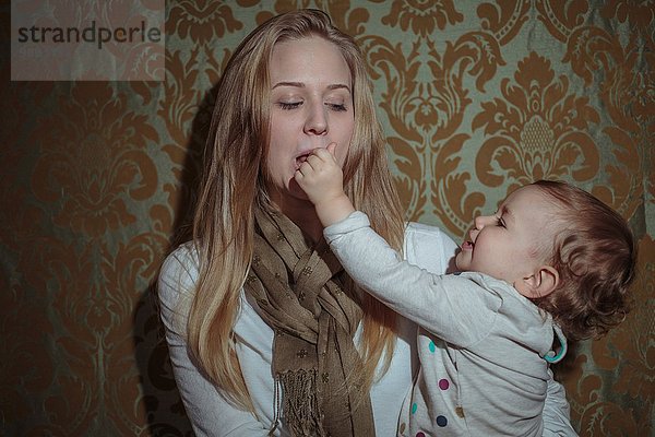 Kleinkind Mädchen  das nach dem Mund der Mutter greift