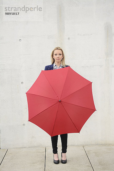 Geschäftsfrau mit rotem Schirm vor der Betonwand