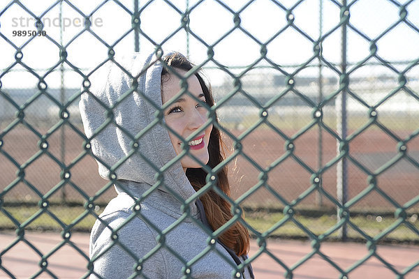 Porträt einer Frau mit Kapuzenjacke hinter Gitterzaun