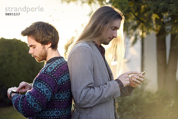 Zwei Hipster Rücken an Rücken mit Smartwatch und Smartphone