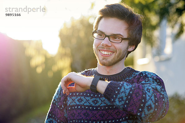 Porträt eines lächelnden jungen Hipsters mit smartwatch im Gegenlicht