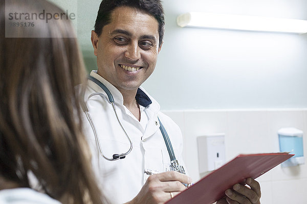 Lächelnder Arzt  der sich Notizen macht  während er dem Patienten zuhört.
