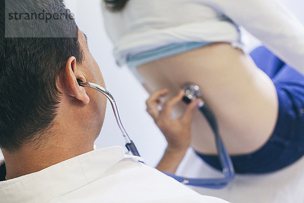 Arzt hört mit Stethoskop auf den Rücken des Patienten