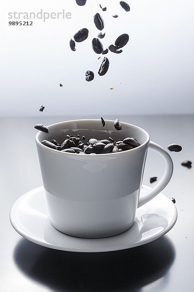 Kaffeebohnen  die in eine weiße Kaffeetasse fallen