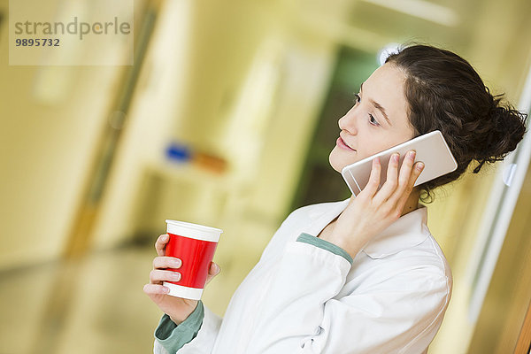 Junger Arzt mit Handy und Kaffeetasse auf dem Krankenhausboden