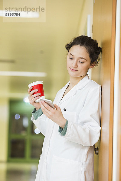 Junger Arzt mit Handy und Kaffeetasse auf dem Krankenhausboden
