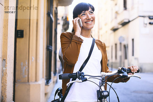 Spanien  Barcelona  lächelnde Frau mit Fahrrad und Handy in der Stadt