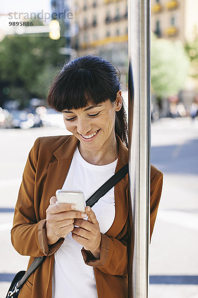 Spanien  Barcelona  Geschäftsfrau mit Smartphone wartet an der Bushaltestelle