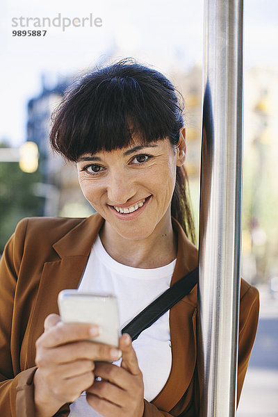 Porträt einer lächelnden Geschäftsfrau mit Smartphone an der Bushaltestelle