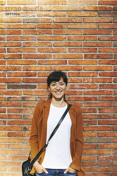 Porträt einer lächelnden Geschäftsfrau vor einer Backsteinmauer