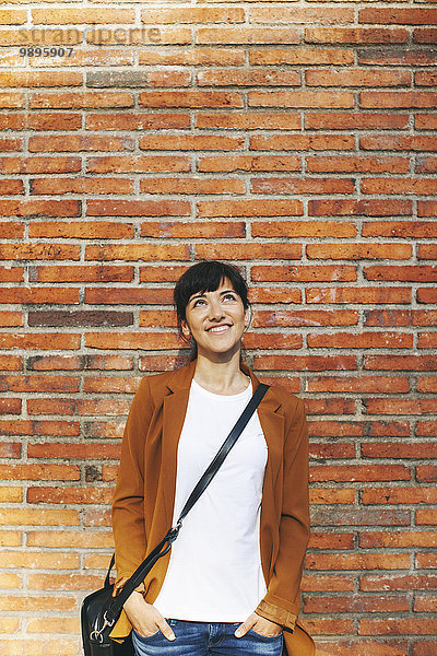 Porträt einer lächelnden Geschäftsfrau vor einer Backsteinmauer