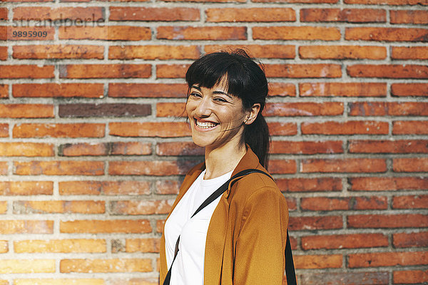 Porträt einer lachenden Geschäftsfrau vor einer Backsteinmauer