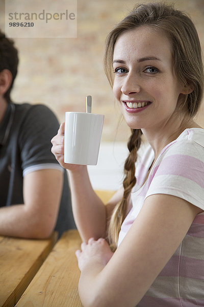 Porträt einer lächelnden jungen Frau beim Kaffeetrinken aus der Tasse