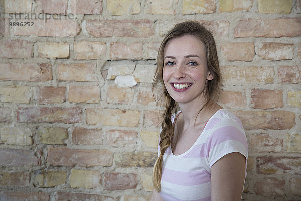 Porträt einer lächelnden jungen Frau vor der Backsteinmauer