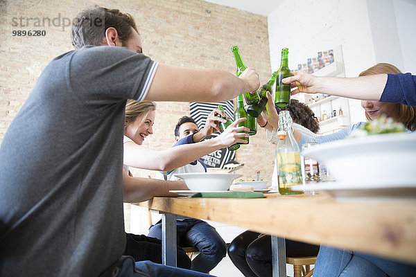Fröhliche Freunde essen zusammen klirrende Bierflaschen