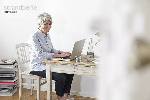 Reife Frau am Tisch sitzend mit Laptop