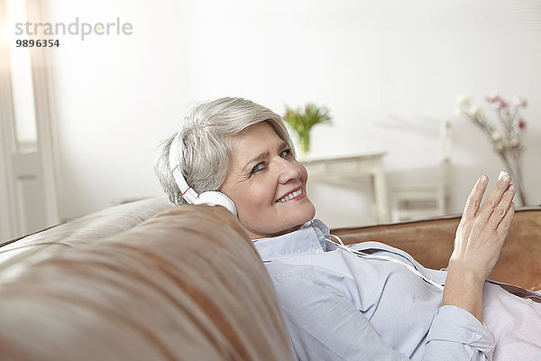 Reife Frau sitzt auf der Couch und hört Musik.