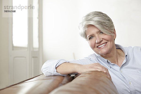 Porträt einer lächelnden reifen Frau  die auf der Couch sitzt