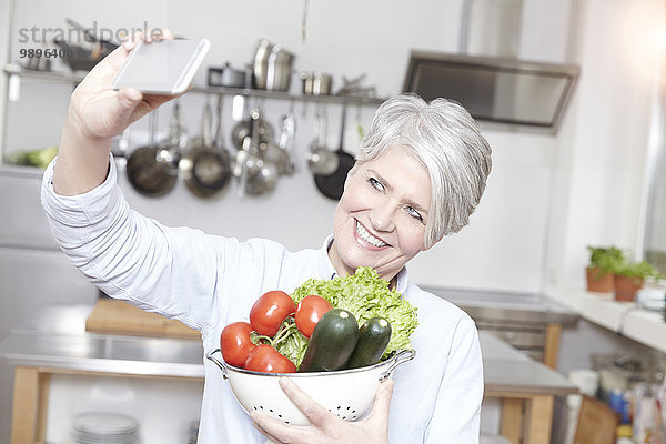 Reife Frau hält Sieb mit Gemüse unter Selbstbedienung