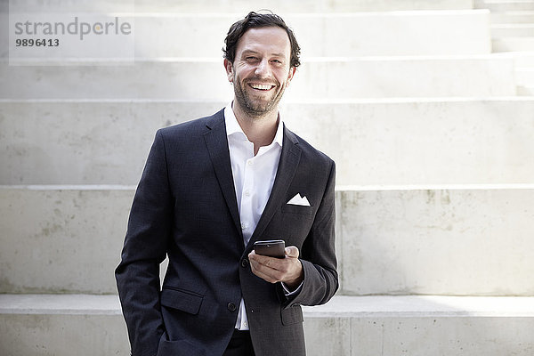 Lächelnder Geschäftsmann mit Smartphone in einem modernen Gebäude