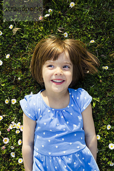 Porträt eines lächelnden kleinen Mädchens auf einer Wiese liegend