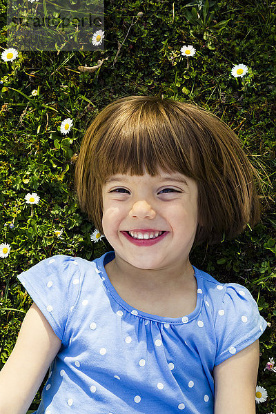 Porträt eines glücklichen kleinen Mädchens auf einer Wiese liegend