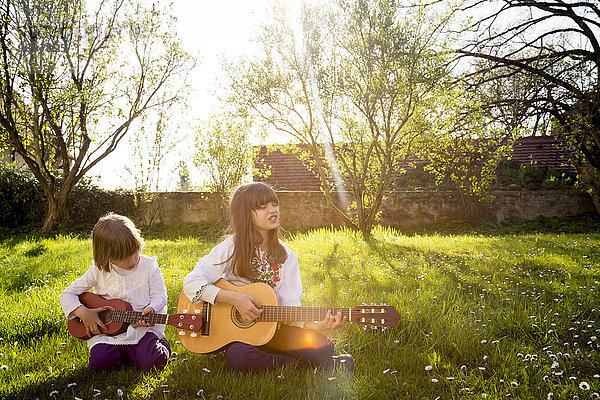 Zwei Schwestern sitzen auf einer Wiese und spielen Gitarre.