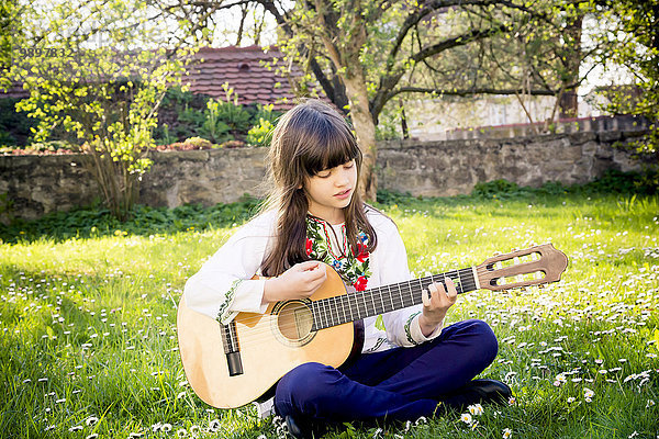 Mädchen sitzt auf einer Wiese und spielt Gitarre.