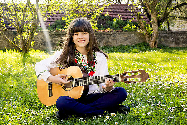 Porträt eines lächelnden Mädchens  das auf einer Wiese sitzt und Gitarre spielt.