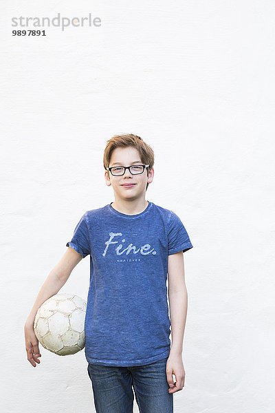 Porträt des Jungen mit Fußball vor weißer Hausfassade