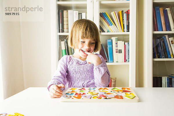Porträt eines lächelnden kleinen Mädchens  das das Alphabet mit Holzbuchstaben lernt.