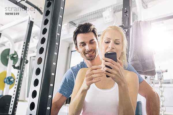 Junges Paar mit Smartphone nach dem Training im Fitnessstudio
