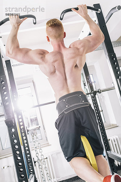 Junger Mann trainiert Klimmzüge auf dem Power Rack im Fitnessstudio