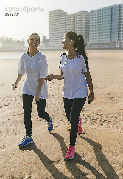 Spanien  Gijon  zwei sportliche junge Frauen mit Ohrstöpseln  die am Strand laufen