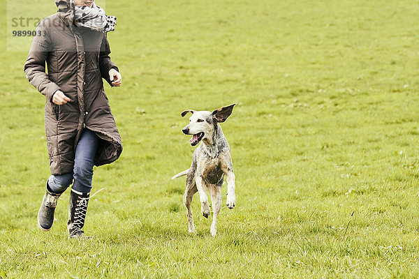 Frau läuft mit Hund auf Wiese
