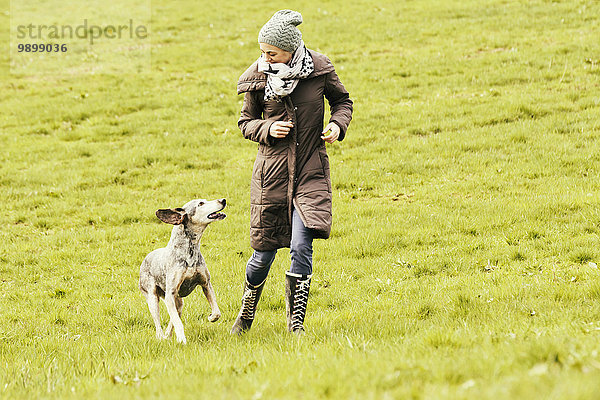 Frau läuft mit Hund auf Wiese