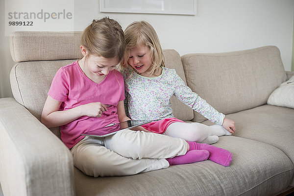 Zwei Schwestern mit digitalem Tablett auf der Couch