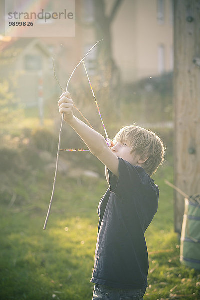 Junge mit selbstgebautem Bogen aus Zweigen und Webstühlen