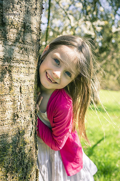 Porträt des lächelnden Mädchens neben Baumstamm