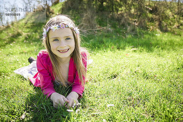 Porträt eines lächelnden Mädchens mit Blumen auf einer Wiese liegend