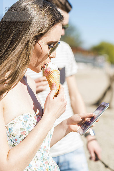 Junges Paar mit Eistüte und Smartphone im Sommer im Freien
