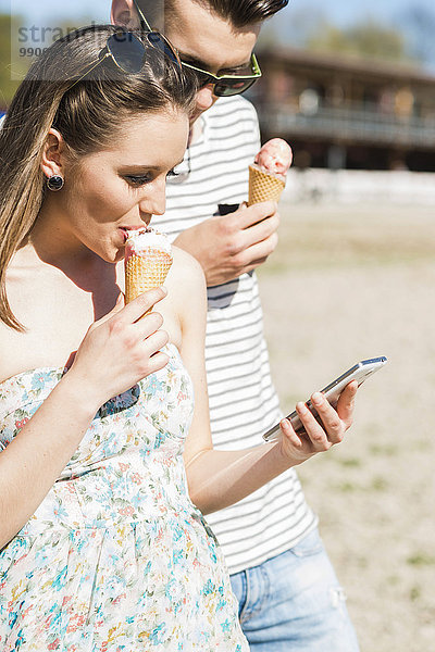 Junges Paar mit Eistüte und Smartphone im Sommer im Freien