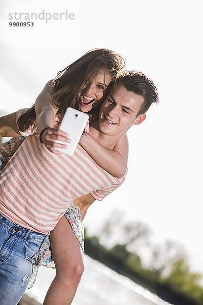 Verspieltes junges Paar mit Selfie im Freien