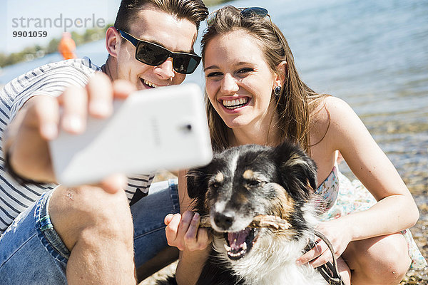 Ein glückliches junges Paar  das sich mit einem Hund am Flussufer vergnügt.