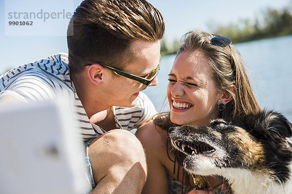 Ein glückliches junges Paar  das sich mit einem Hund am Flussufer vergnügt.