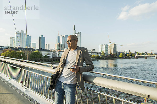 Deutschland  Frankfurt  Geschäftsmann auf Brücke mit Aktentasche und Smartphone