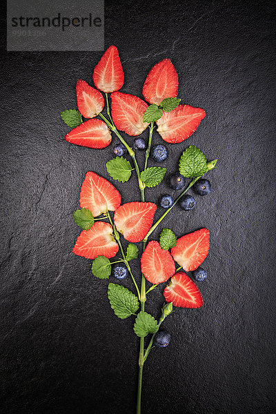 Symbolische Blume in Form von geschnittenen Erdbeeren  Melisse und Blaubeeren auf Schiefer